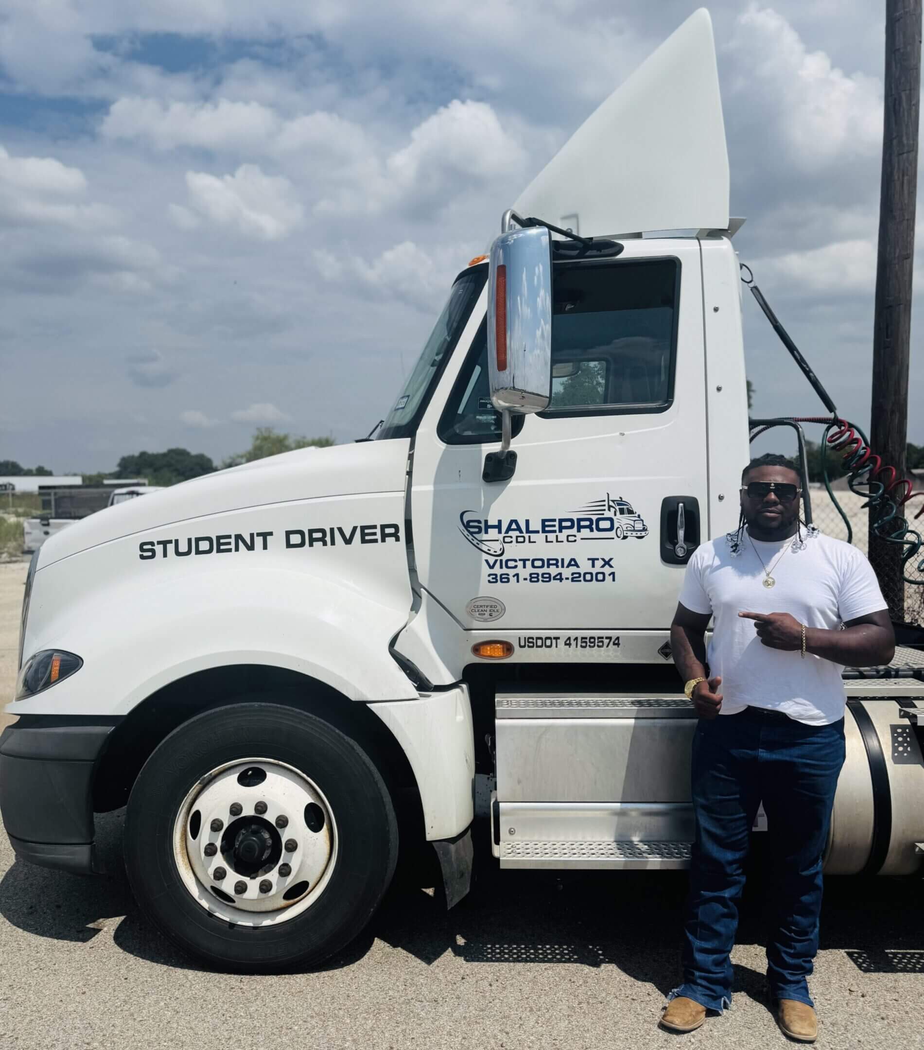 Student driver standing beside a large white truck on a cloudy day.
