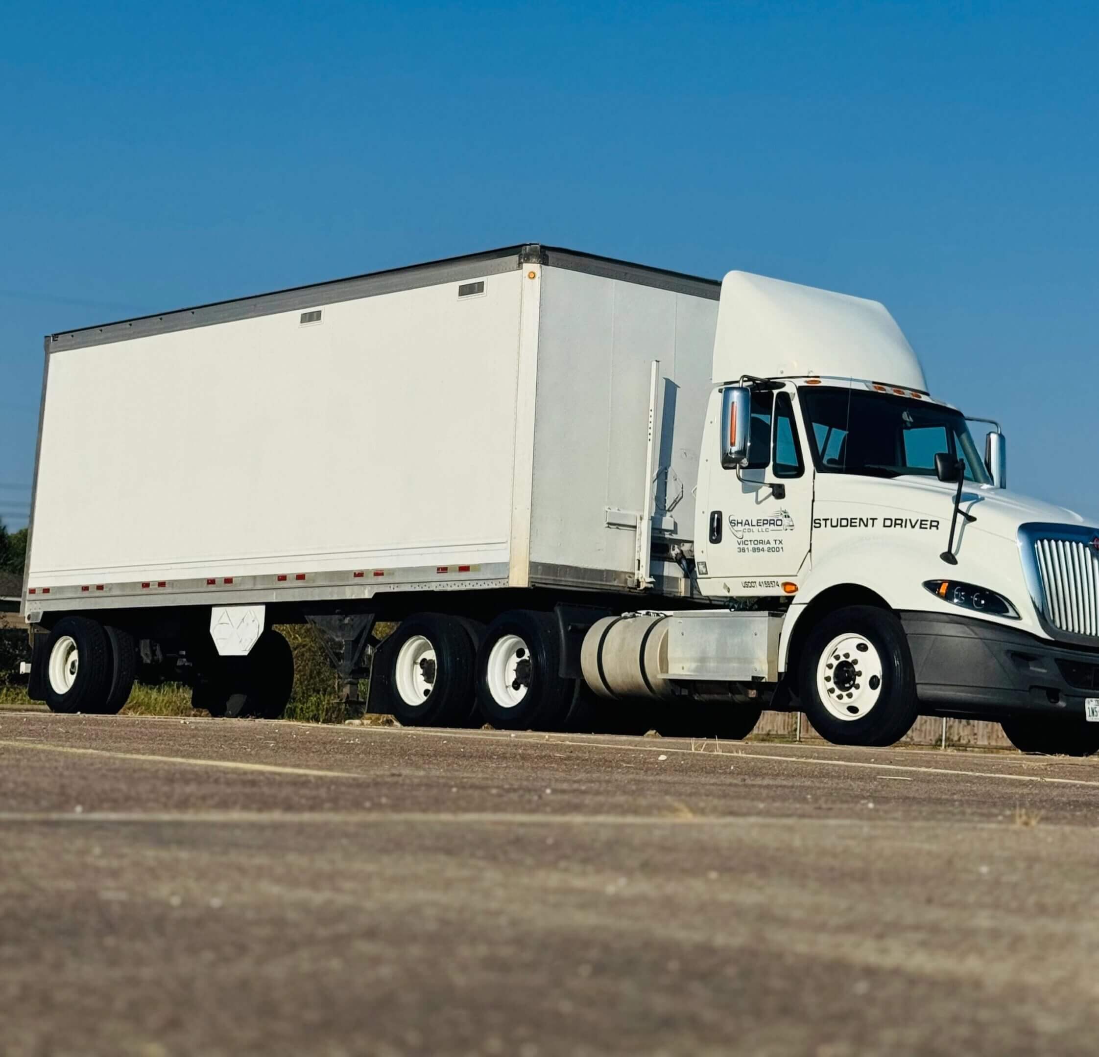 A large white semi-truck with a trailer parked on an open road under a clear blue sky.