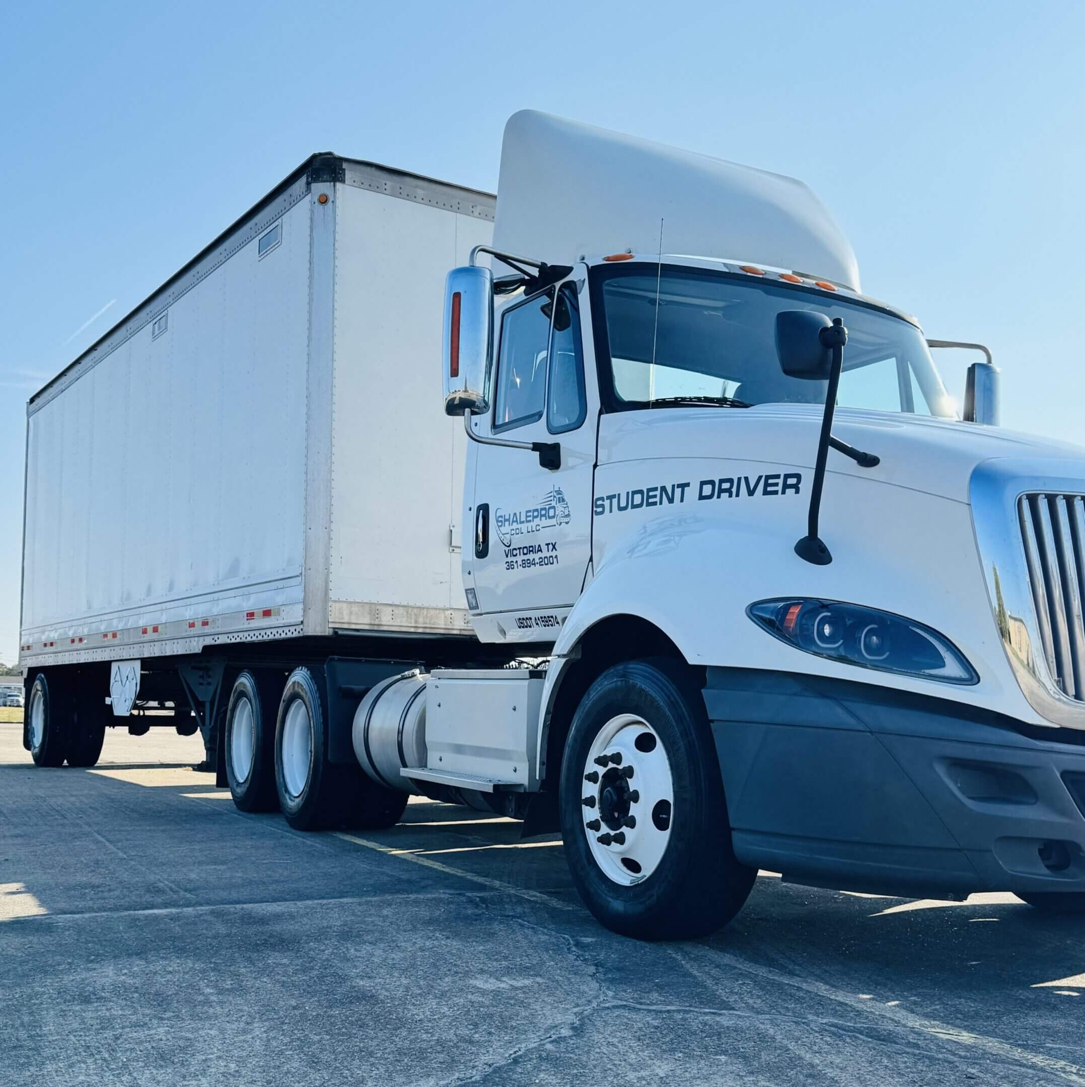 White semi-truck parked on asphalt under clear blue sky.