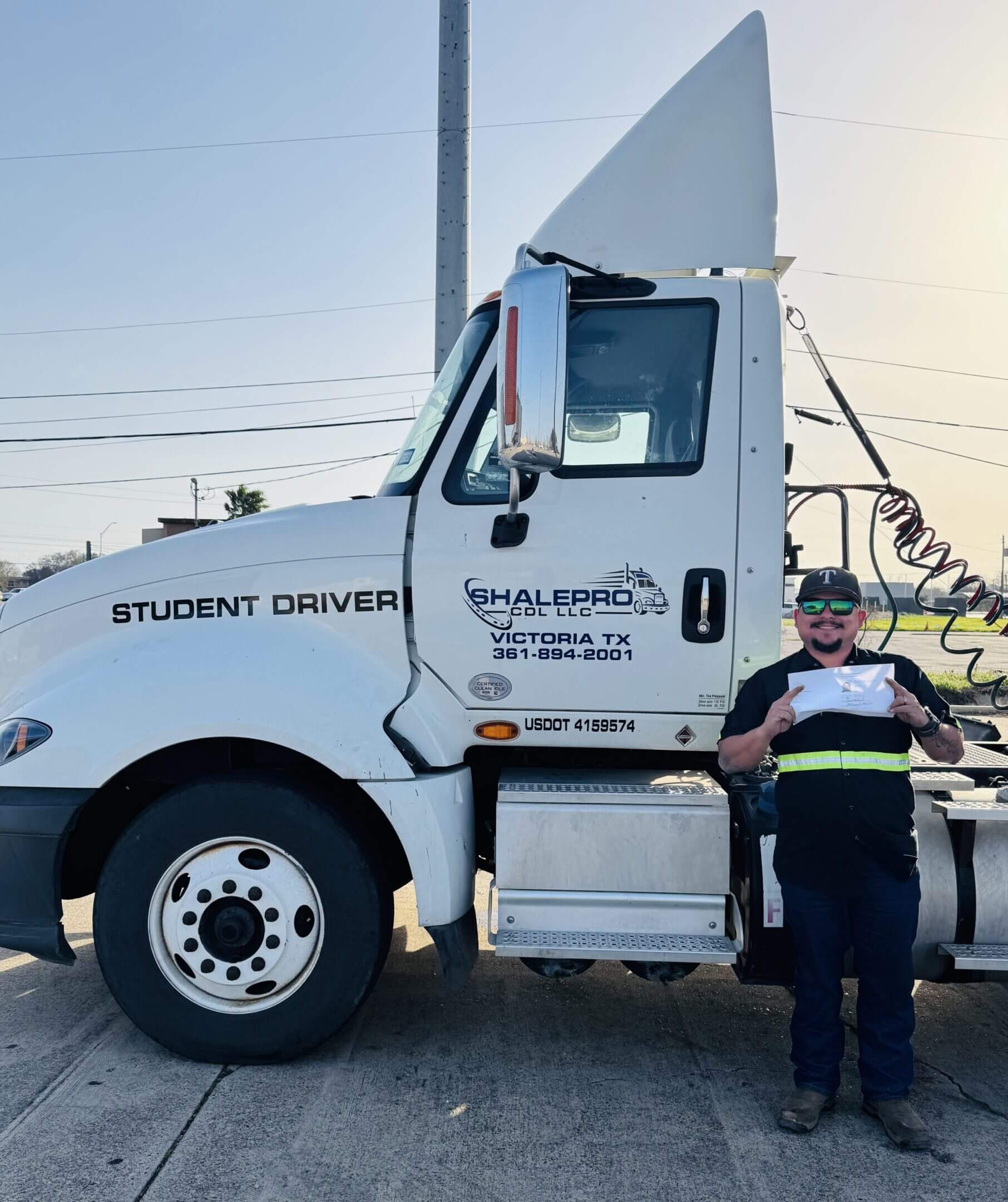 A truck driver standing beside a large white tractor truck labeled 'Student Driver.'